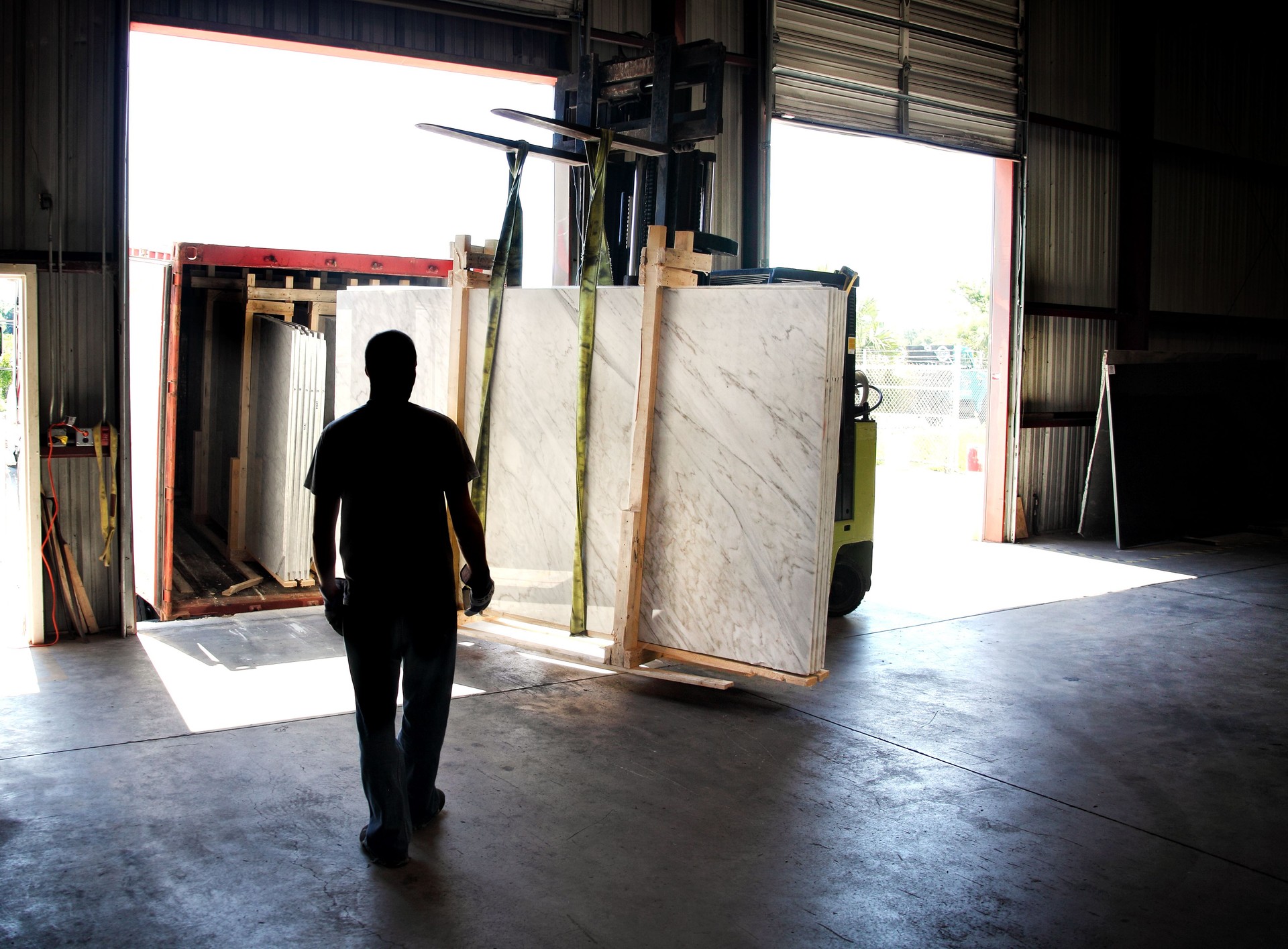 Worker lifting and carrying granite slabs by forklift at warehouse